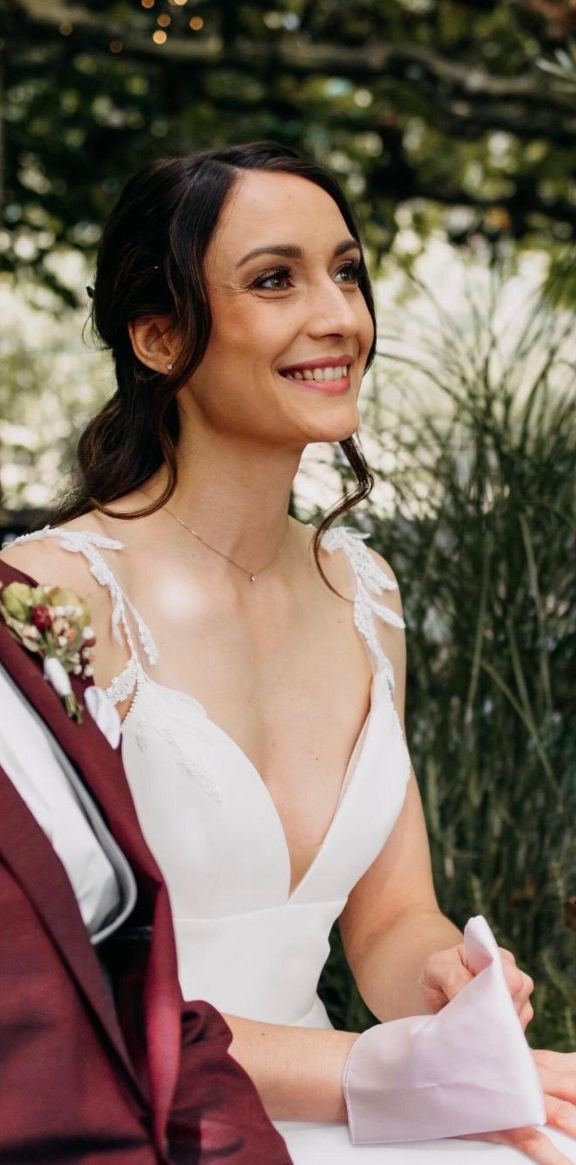Lachende Braut im Garten mit weich zurückgenommenem Haar und natürlichem Make-up