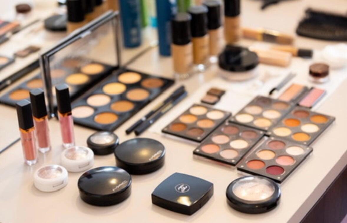 Aufgeklappte Make-up-Paletten, Pinsel, Foundations und Lipglosse auf einem hellen Tisch