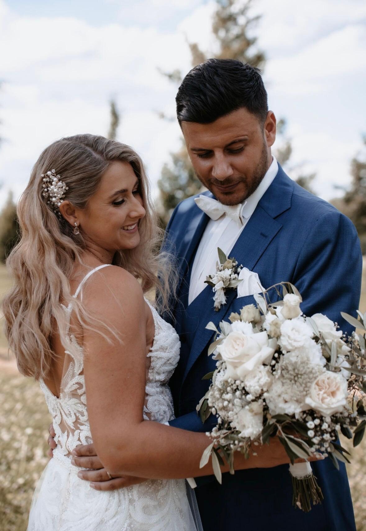 Brautpaar im Freien, halboffene Brautfrisur mit floralem Haarschmuck, weißer Brautstrauß
